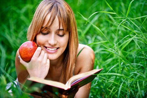 Ragazza legge un libro su un prato con una mela in mano