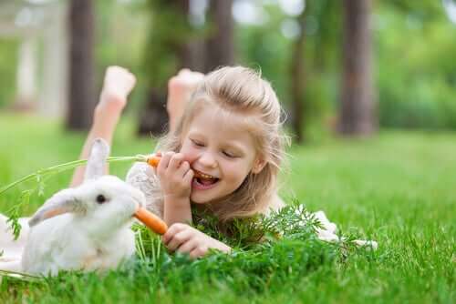 Bambina che mangia le carote con un coniglio.